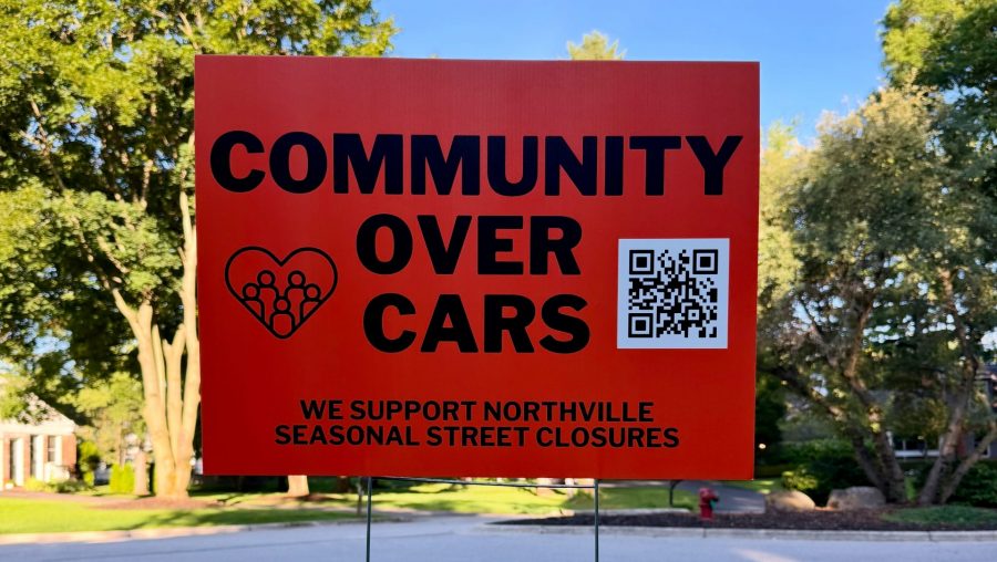 An orange yard sign says "community over cars."