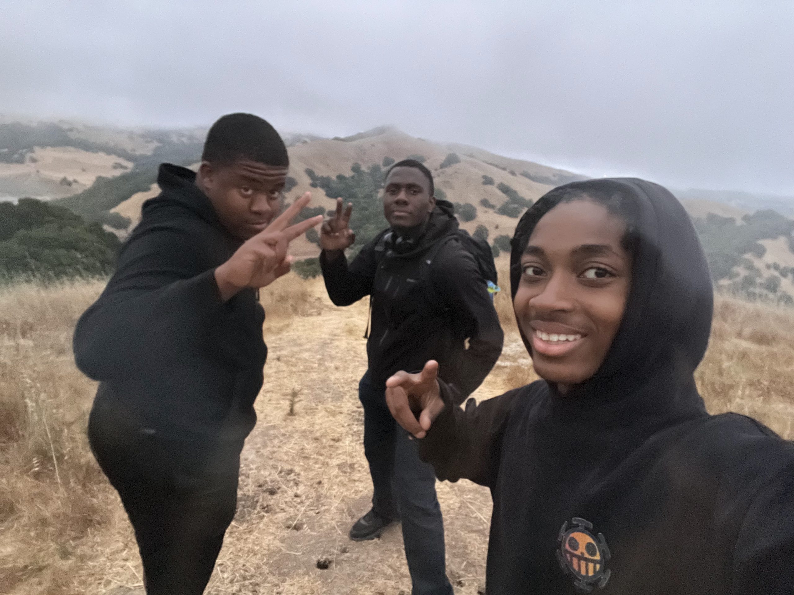 Three students pose on top of a mountain