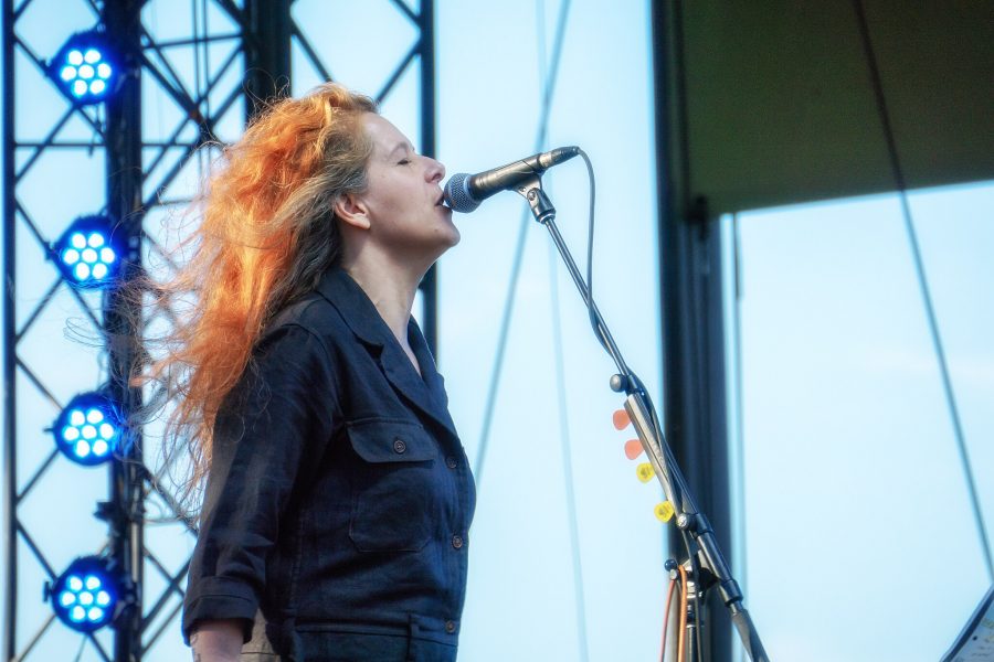 A women performs on stage with her hair blowing in the wind and a lighting stand is behind her.
