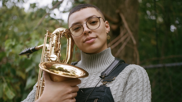 Kaleigh Wilder is outside holding her saxophone near her face.