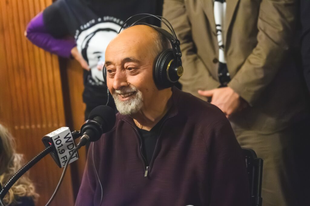 Ismael Ahmed talks to Ann Delisi and Don Was. He is seated behind a microphone