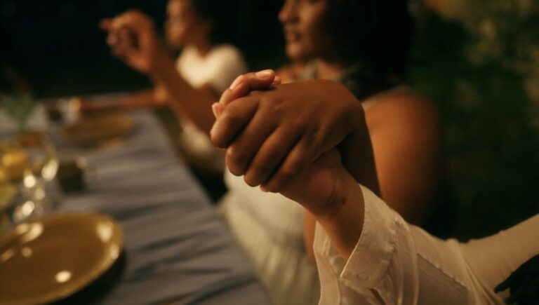 People join hands in prayer around a dinner table.