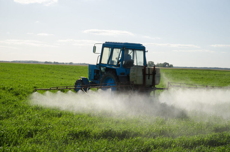 A tractor sprays a mist of herbicide, insecticide or fertilizer on an expanse of green crops.