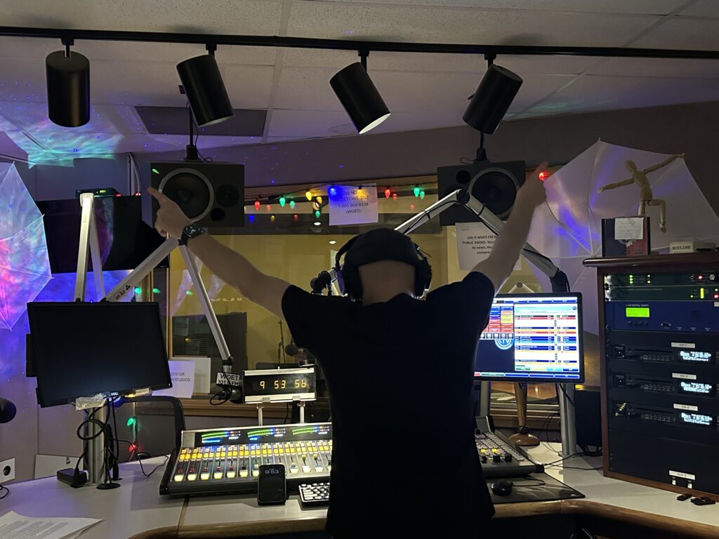 Host Darren Revell points to the ceiling in front of the soundboard as he plays a track.