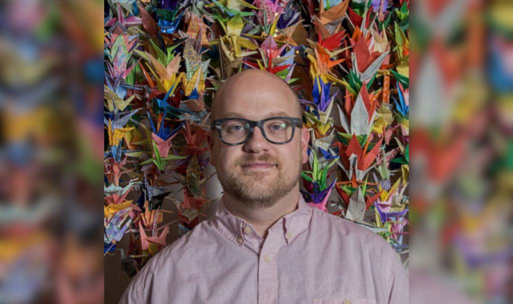 Jeremy Peters in a pink collared button up in front of a curtain of paper cranes.