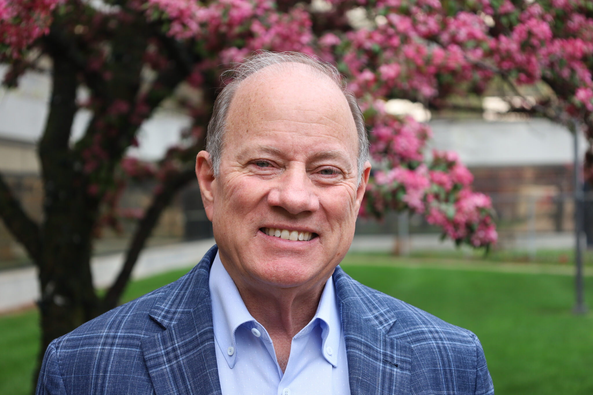 Mike Duggan is outside on a spring day in front of a blooming tree with purple flowers
