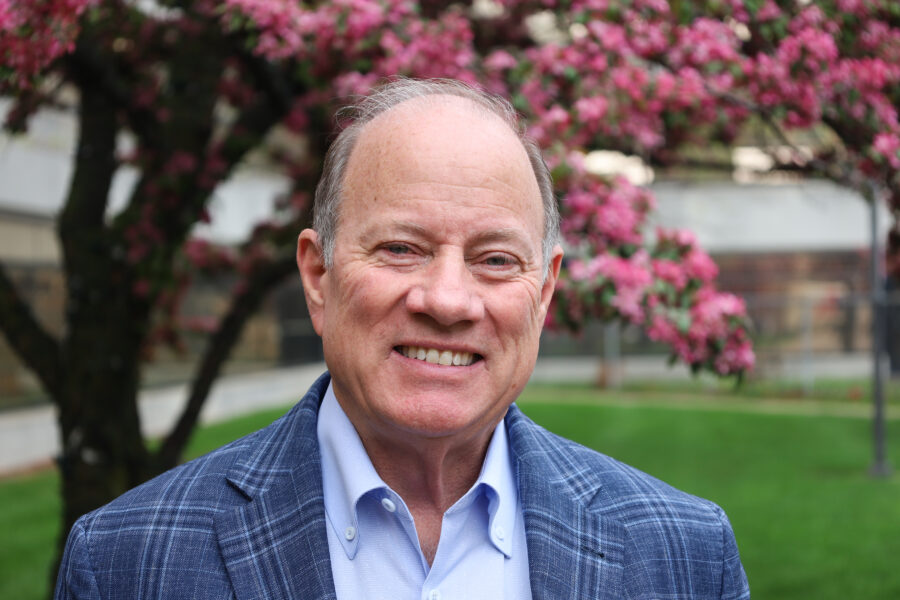 Mike Duggan is outside on a spring day in front of a blooming tree with purple flowers