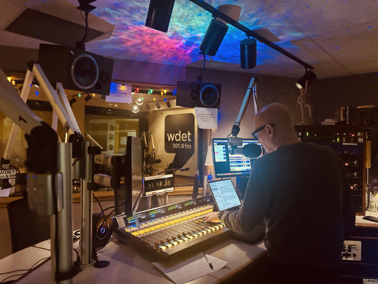 Darren Revell in front of the sound board at WDET studio. Lights cast patterns on the ceiling.