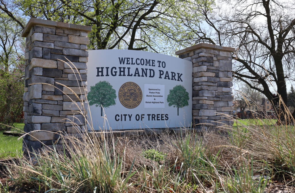 A sign that reads "Welcome to Highland Park, City of Trees" surrounded by wild grasses.