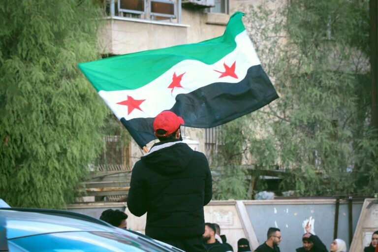A man in a red baseball cap holds the Syrian flag.