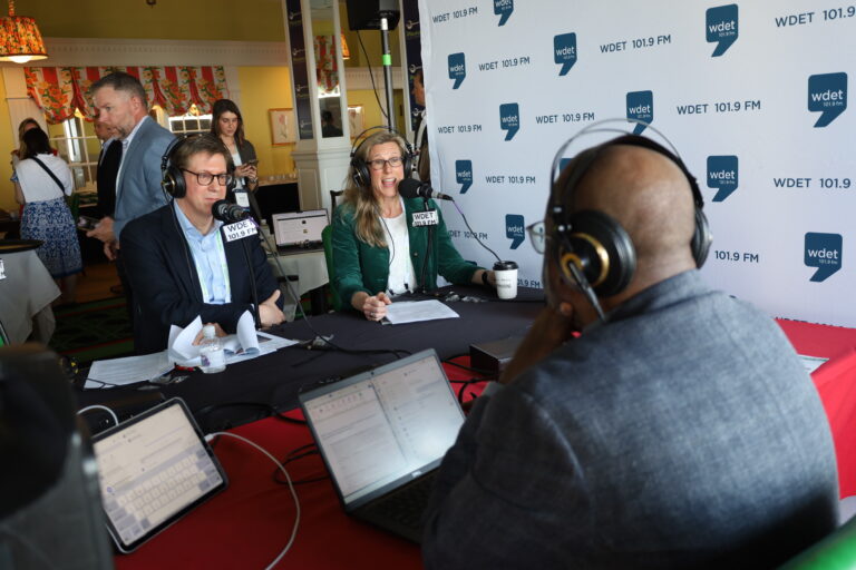 A man and woman sit across from a reporter for a radio interview.