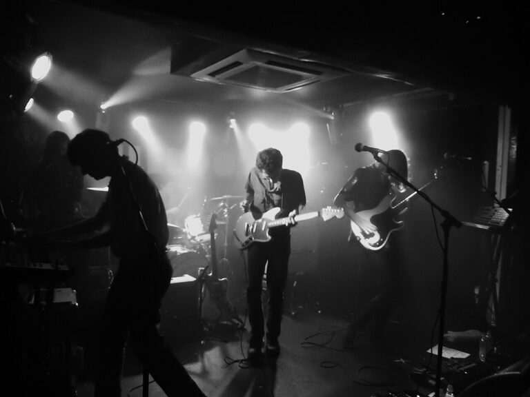Band performs on stage with stark spotlighting.