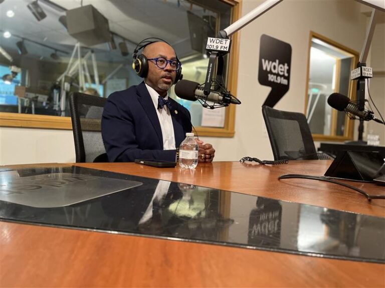William McConico in front of studio mic, wearing headphones with a sport jacket, button up and bow tie.