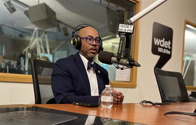 William McConico in front of studio mic, wearing headphones with a sport jacket, button up and bow tie.