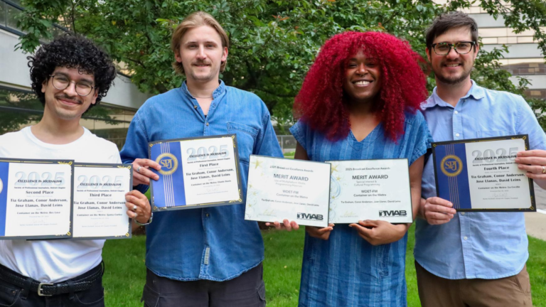 Four people stand outside holding folders with theirs awards in them.