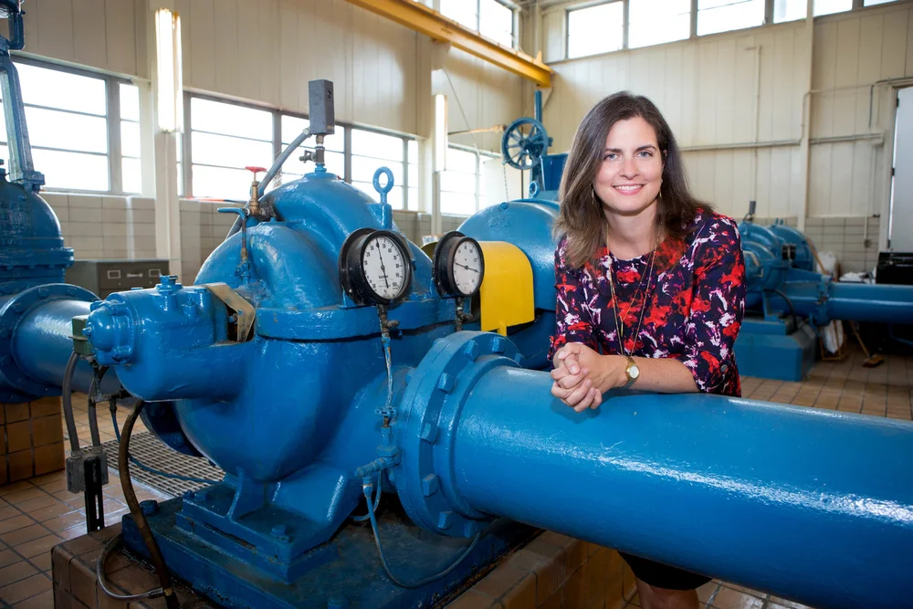 Erin Warn Betanzo leans posted on a large plue water pipe.