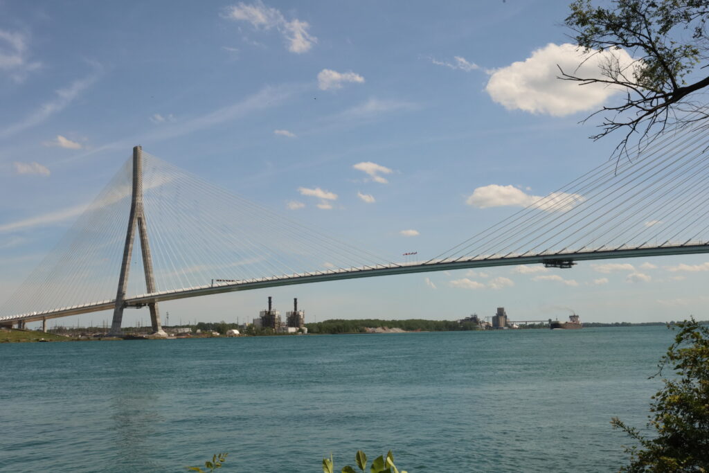 The Gordie Howe Bridge stretches across Detroit River, with a blue sky behind it.
