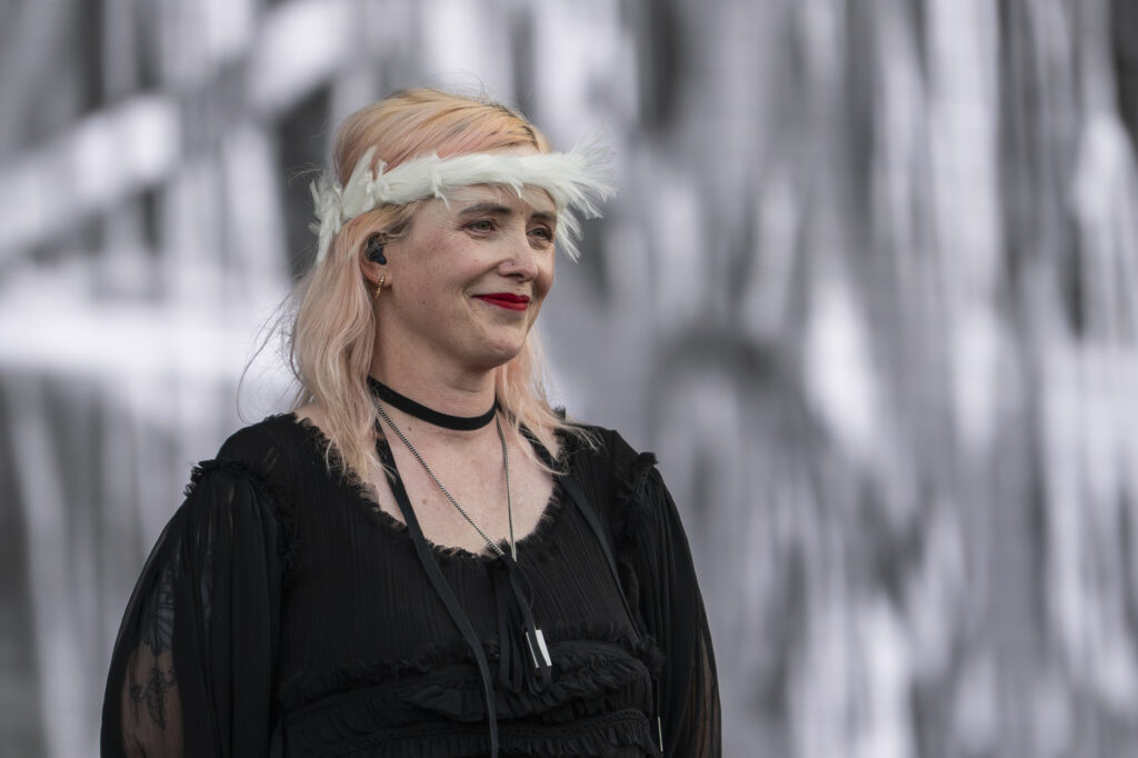 White woman in black flowy shirt smiles, wearing a white-feathery crown.