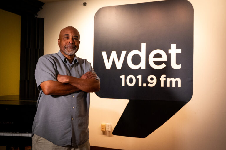 Kim Hunter stands with arms crossed to the left of the WDET logo.