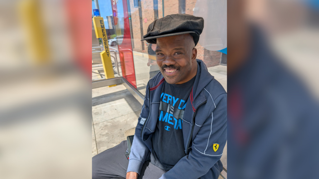 George Thompson smiles at the camera, seated at a QLine stop.