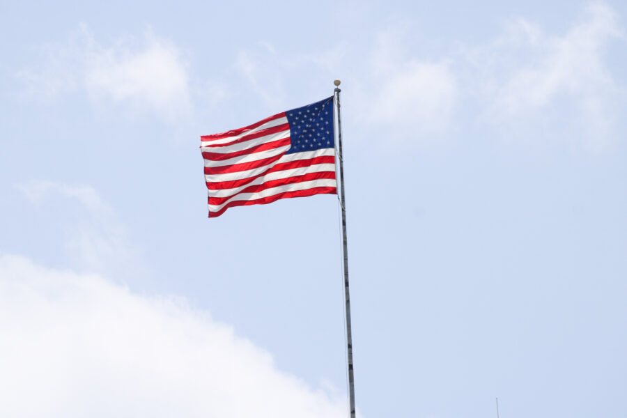 Left facing American flag flying in the wind atop a flagpole.