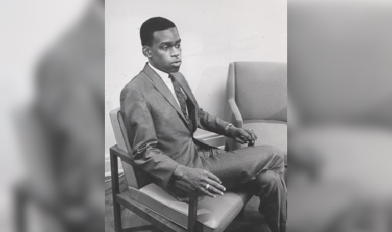 A black and white portrait of a young Jay Butler, sitting in a suit.