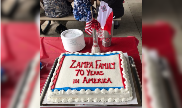 A white cake with text "Zampa Family 70 Years in America" with an American and Maltese flag.