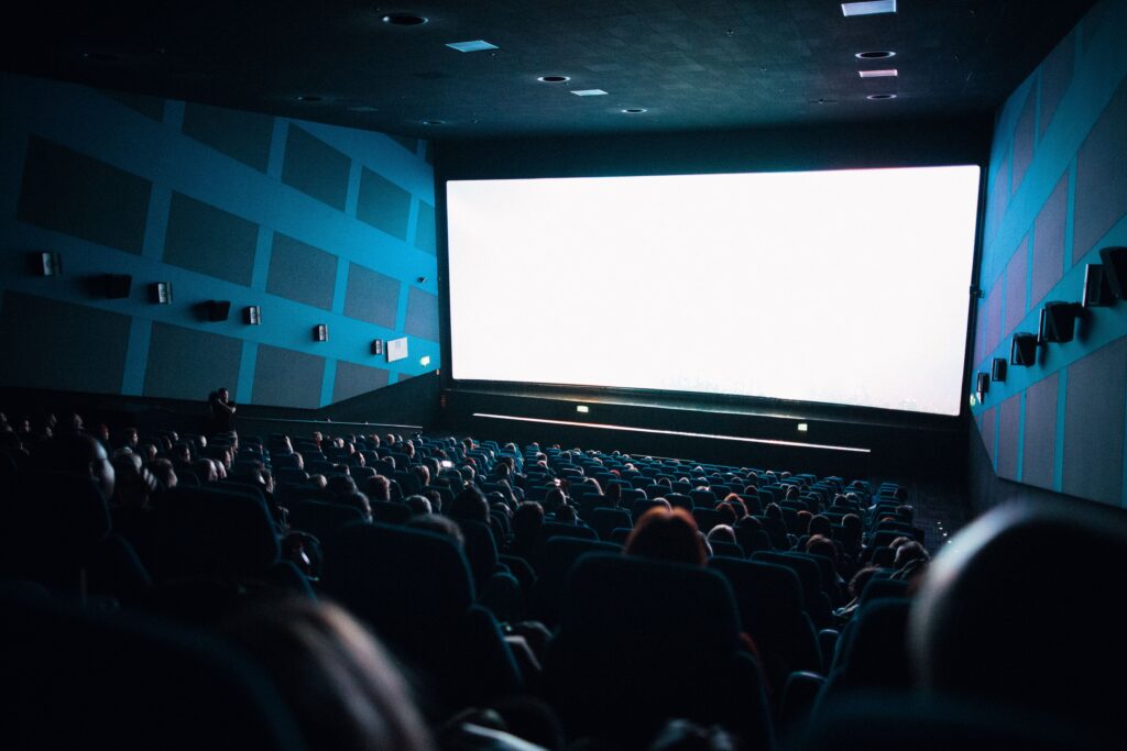 A white movie theater screen glows in front of a crowded audience.