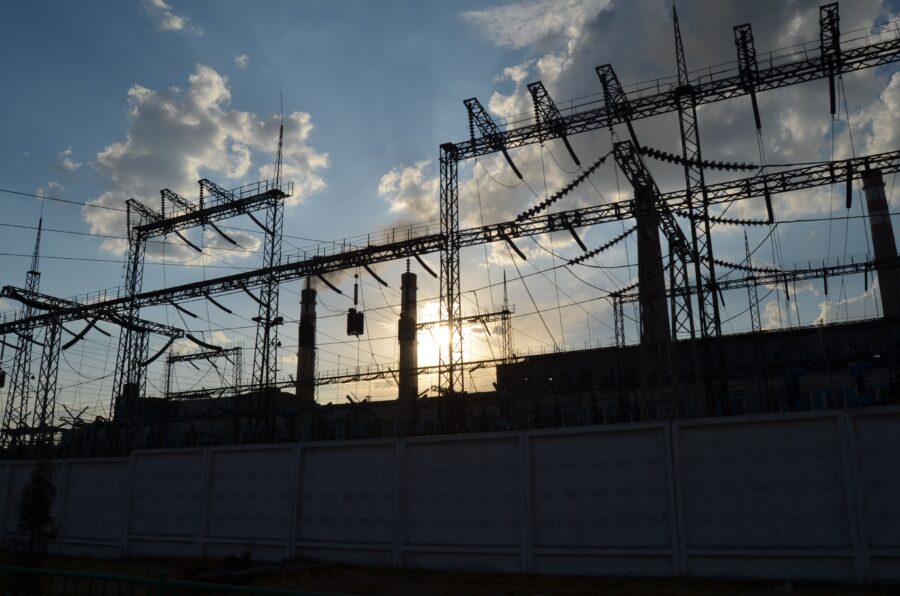 A power substation in front of a low sun. The sky is blue with some clouds.