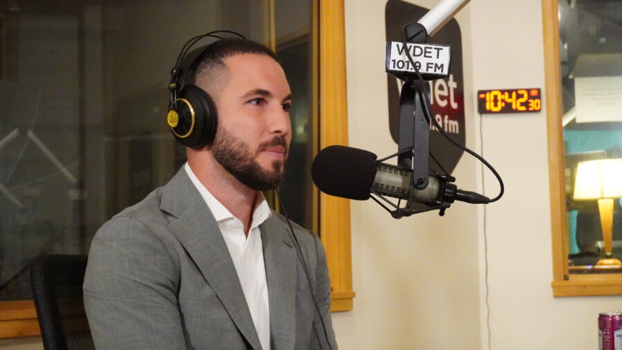 Mayor Hammoud, face in profile in front of a microphone in WDET studios. He's wearing headphones, a white button up and a gray sports coat.
