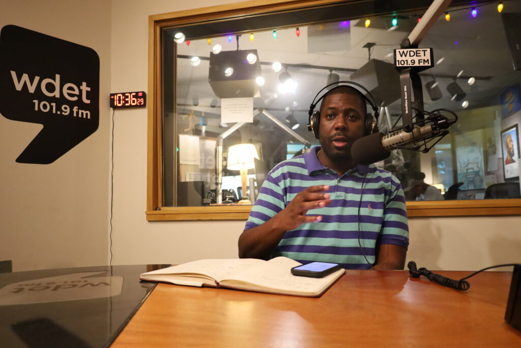 Branden Snyder in WDET studios speaks into the mic, gesturing with his hand.