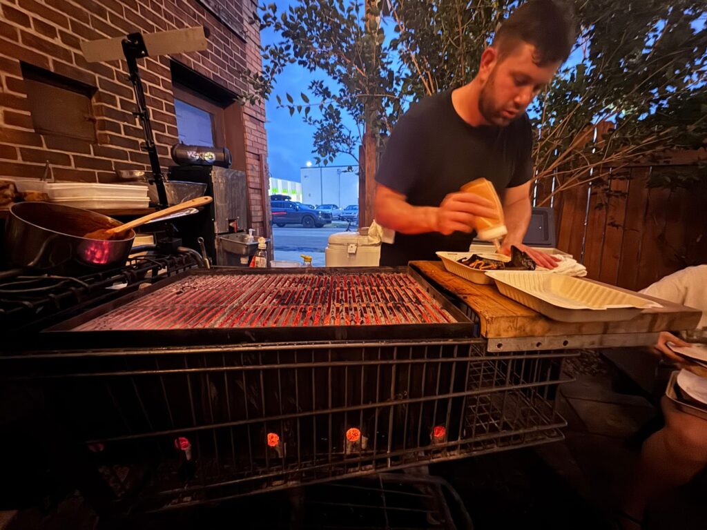 Chef Andrew Stevick uses a bottle to drizzle chipotle sauce on a dish in a disposable take-out box.