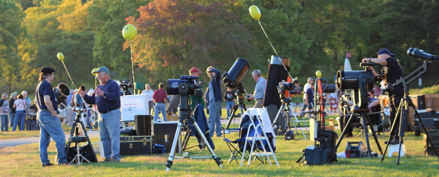 People mill about on the grass between large telescopes to view outer space.