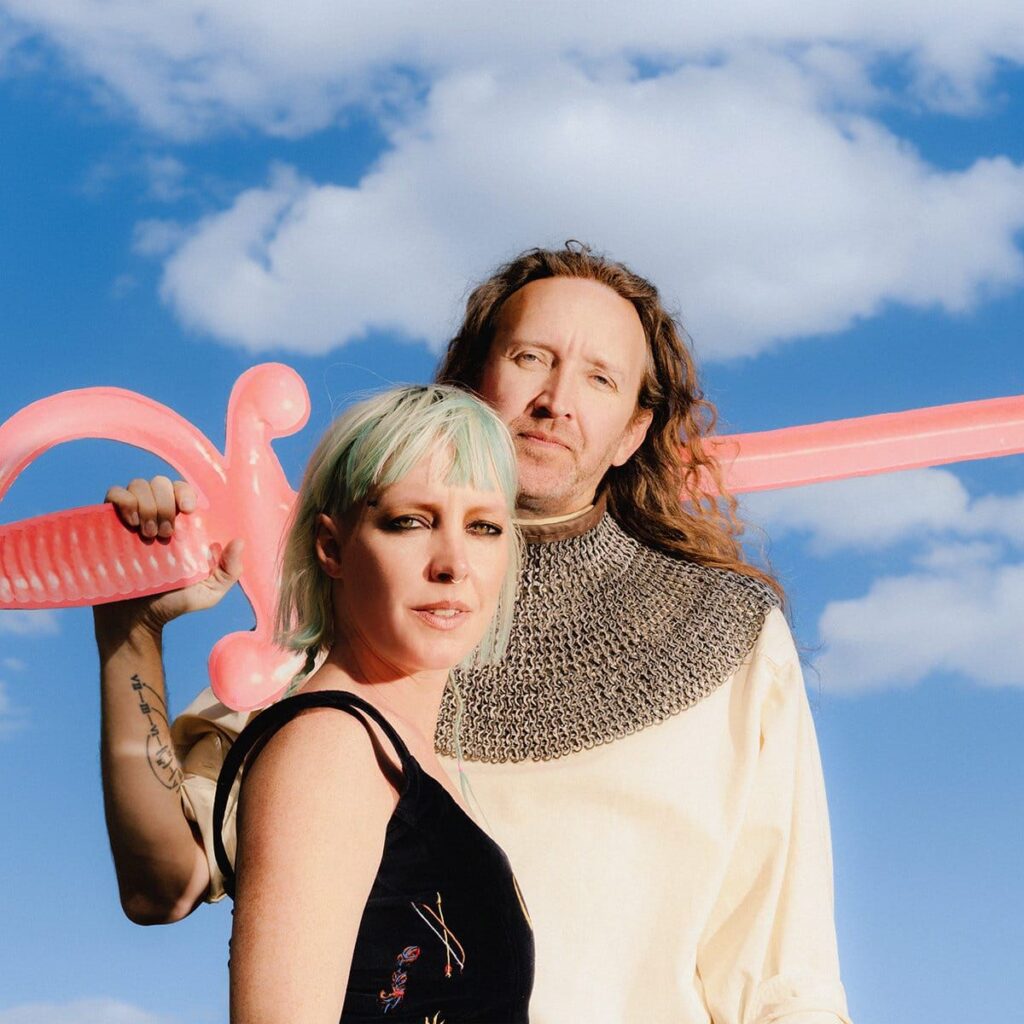 Sylvan Esso in front of a blue sky backdrop with clouds.